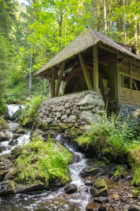 Historische Wassermühle mit Mühlrad an einem Gebirgsbach im Schwarzwald, umgeben von Felsen und Wald