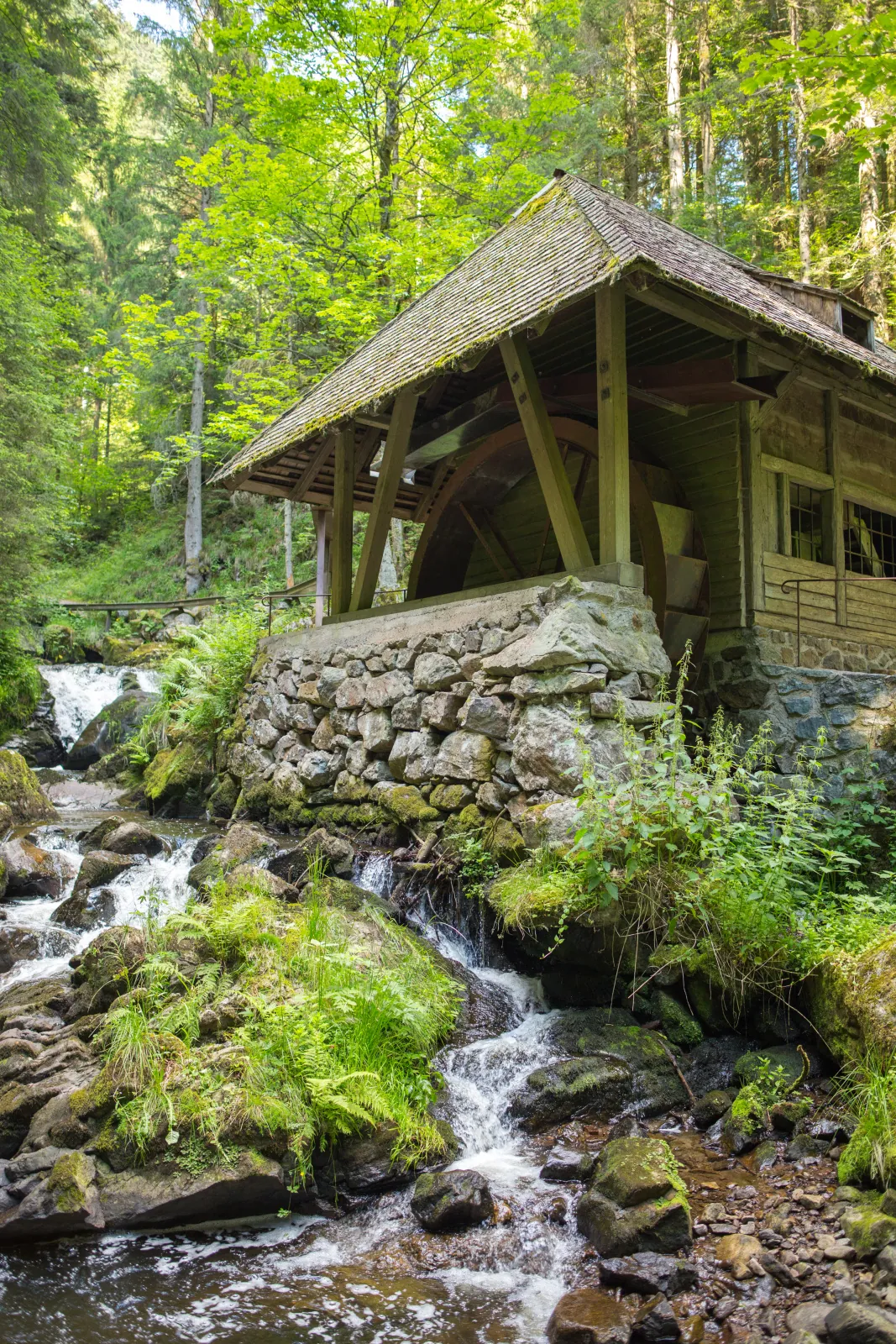 Historische Wassermühle mit Mühlrad an einem Gebirgsbach im Schwarzwald, umgeben von Felsen und Wald