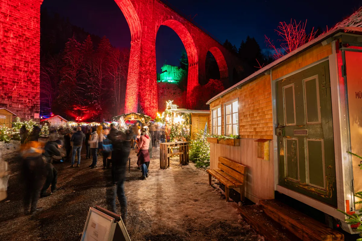 Weihnachtsmarkt in der Ravennaschlucht bei Nacht, rot beleuchtetes Viadukt, Burg im Hintergrund
