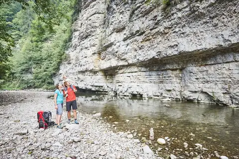 Familie an Kiesufer der Wutach, dahinter senkrechte Kalksteinfelsen und klares Wasser