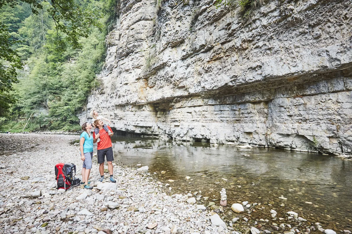 Familie an Kiesufer der Wutach, dahinter senkrechte Kalksteinfelsen und klares Wasser