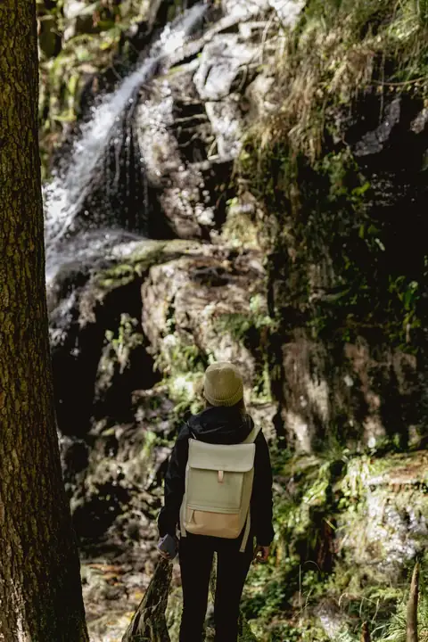 Wanderin mit Rucksack betrachtet einen Wasserfall zwischen bemoosten Felsen im Schwarzwald
