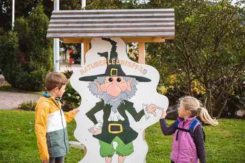 Zwei Kinder stehen vor einer bemalten Holzfigur mit der Aufschrift Naturerlebnispfad in Hinterzarten