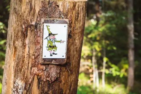 Holzschild mit Comicfigur eines Waldgeistes an einem Baumstamm im Schwarzwald