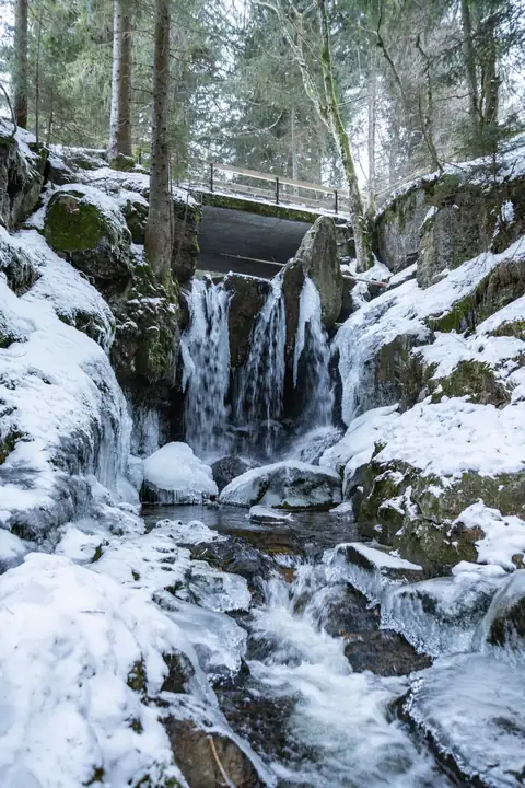 Menzenschwander Wasserfall im Winter mit Eisformationen und Schnee, Holzbrücke im Hintergrund