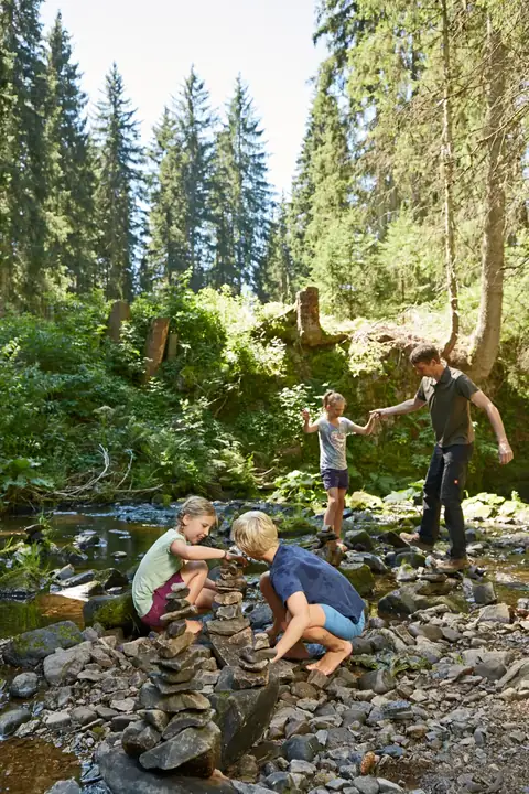 Familie spielt an einem Gebirgsbach im Schwarzwald, Kinder stapeln Steine, Vater hält Tochter die Hand