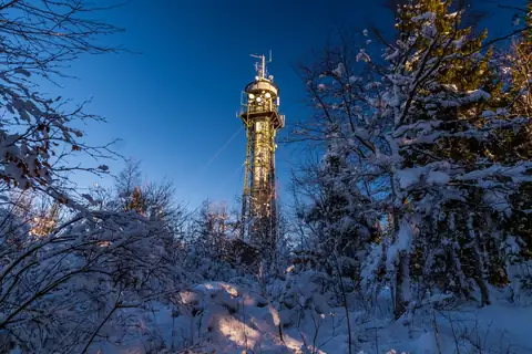 Schneebedeckter Aussichtsturm Hochfirst mit Antennen, umgeben von verschneiten Bäumen bei Dämmerung