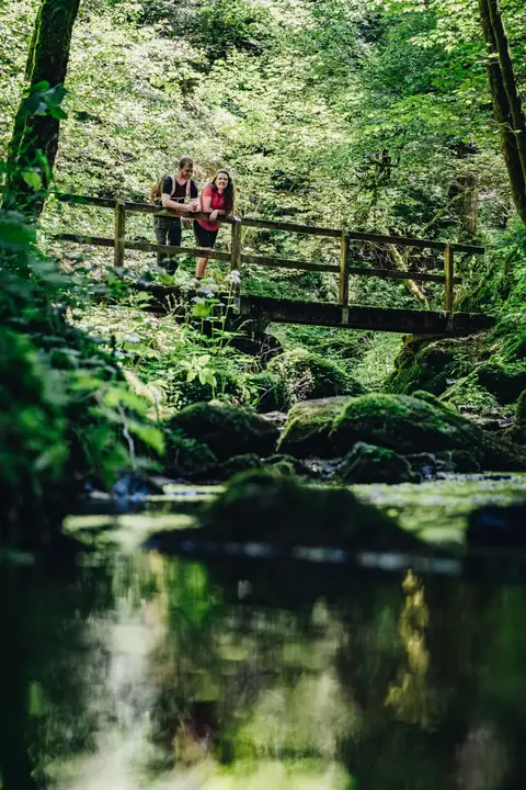 Wanderpaar auf einer Holzbrücke über einen moosigen Bach in der Lotenbachklamm