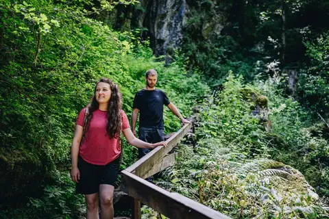 Zwei Wanderer überqueren eine Holzbrücke in der grünen, felsigen Lotenbachklamm