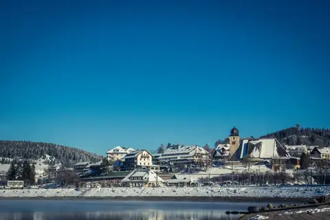 Verschneites Ortspanorama von Schluchsee mit Kirchturm, gesehen über den zugefrorenen See