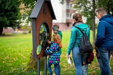 Familie mit zwei Kindern an einer Erlebnisstation mit sichtbarem Zahnradwerk auf dem Kuckucksuhrenpfad