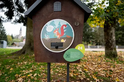 Rostige Stationsbox in Hausform mit Eichhoernchen-Illustration, Muenzschlitz und 2-Euro-Hinweis im herbstlichen Park