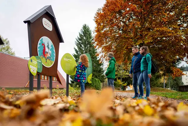 Eine Familie liest sich die Willkommenstafel am Beginn des Kuckucksuhrenpfad in Schönwald durch.