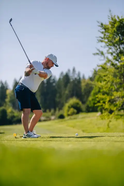 Golfspieler beim Abschlag mit Blick auf Fairway und Waldkulisse