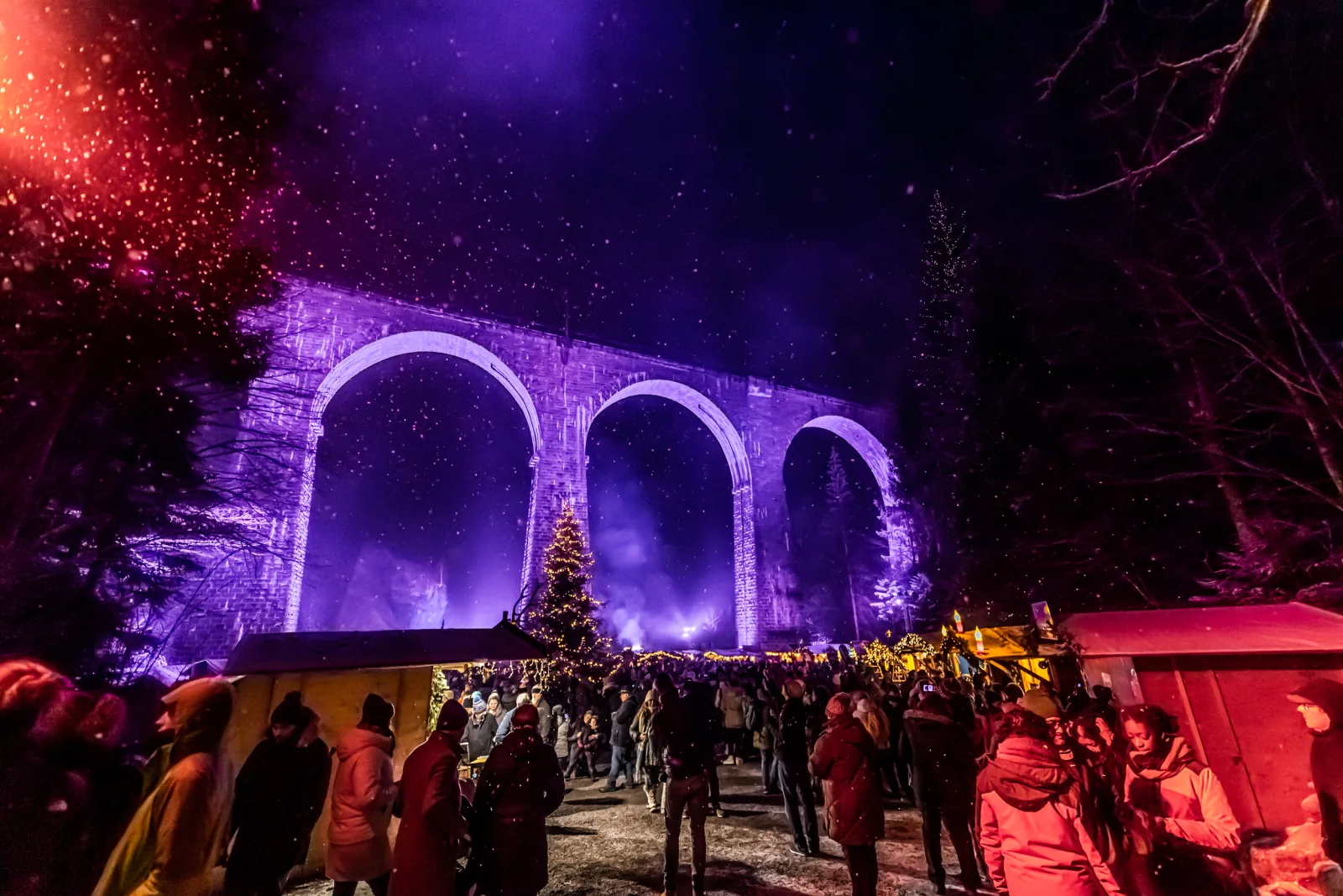 Der Weihnachtsmarkt in der Ravennaschlucht mit dem violett angestrahlten Ravennaviadukt im Hintergrund.