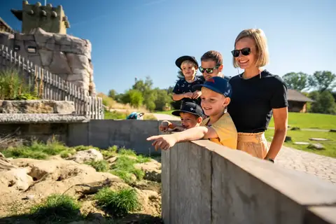 Familie mit drei Kindern lehnt an einer Steinmauer und zeigt auf ein Tiergehege im Freizeitpark Tatzmania