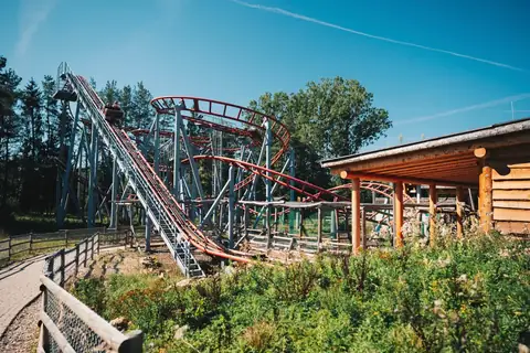 Achterbahn mit roter Schiene und grauer Stahlkonstruktion im Freizeitpark Tatzmania, sonniger Tag