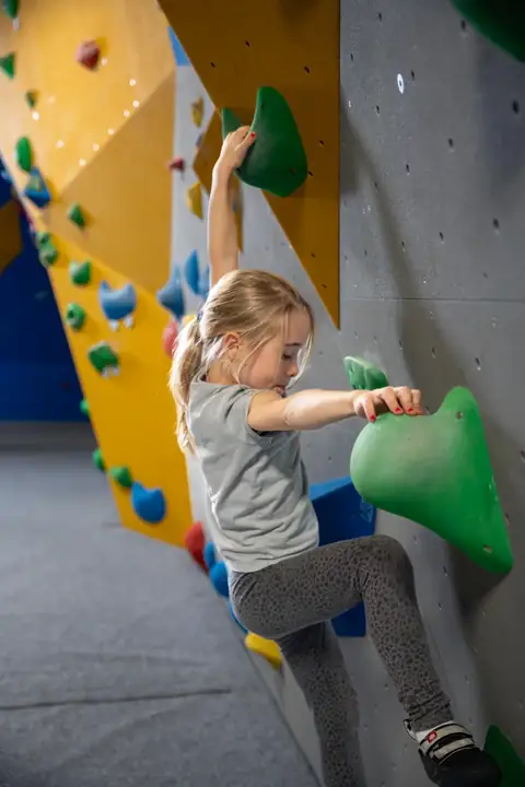 Kind klettert an bunter Boulderwand mit grünen Griffen in der Kletterhalle