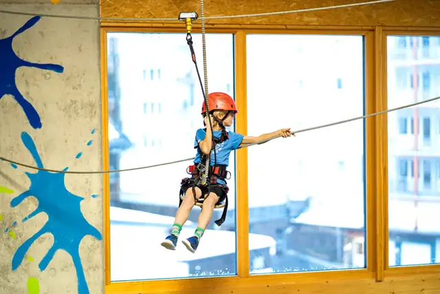 Ein Kind rutscht auf einer Seilrutsche im Indoor Hochseilgarten in der Indoor Spiel- & Sporthalle Fundorena