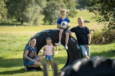Familie posiert an einem großen liegenden Traktorreifen auf einer Wiese