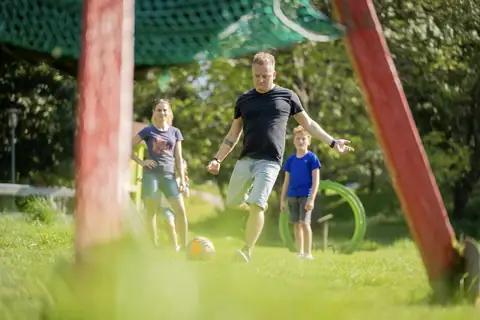Familie spielt Fußball vor einem Fußballtor mit grünem Netz auf einer Wiese