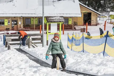 Kind mit Bob auf Förderband im Schnee vor Hütte am Spaßpark Hochschwarzwald