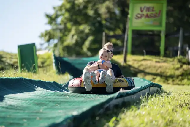 Vater und Tochter rutschen im Doppel-Reifen eine Sommerrodelbahn hinunter