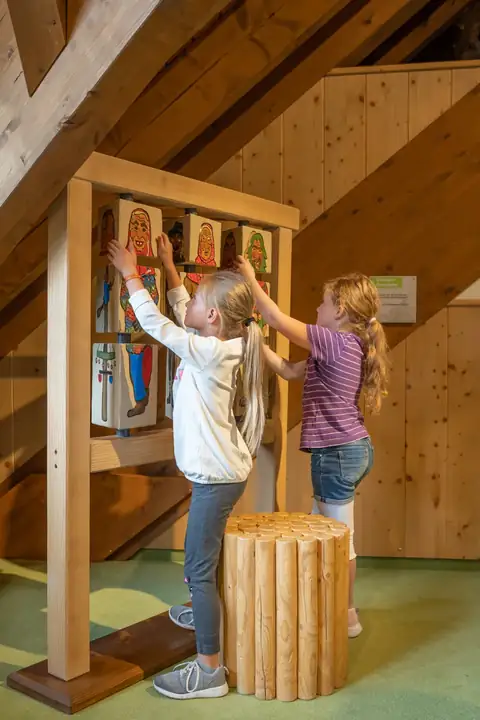 Zwei Mädchen spielen an einem Drehpuzzle mit bemalten Figuren in einem Holzgebäude