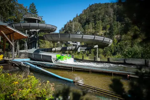 Grünes Boot auf der Wildwasserbahn des Steinwasen-Parks mit Wasserspritzer, Schwarzwald im Hintergrund