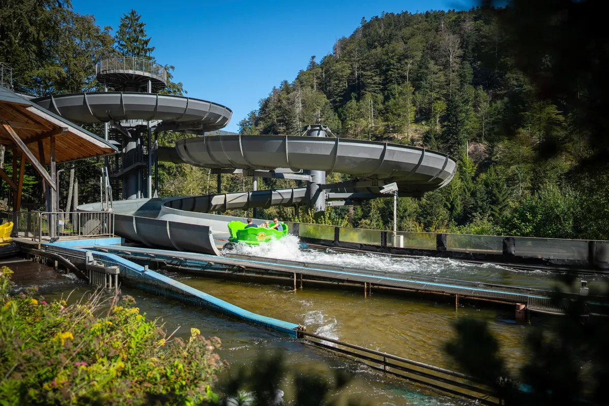 Grünes Boot auf der Wildwasserbahn des Steinwasen-Parks mit Wasserspritzer, Schwarzwald im Hintergrund