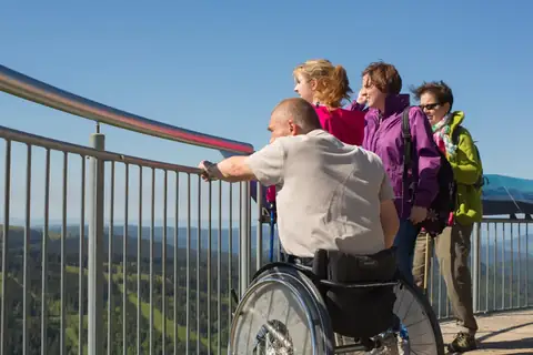 Gruppe von Besuchern auf einer Aussichtsplattform mit Panoramablick über den Schwarzwald, darunter ein Rollstuhlfahrer