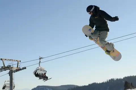 Snowboarder springt hoch über einen Skilift am Feldberg, Schwarzwald im Hintergrund