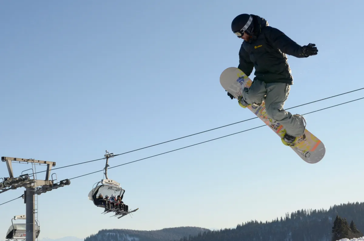 Snowboarder springt hoch über einen Skilift am Feldberg, Schwarzwald im Hintergrund