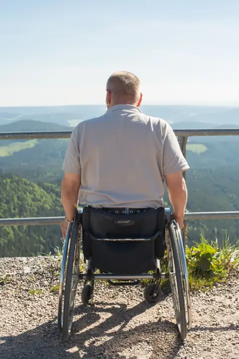 Mann im Rollstuhl von hinten an Aussichtsplattform mit Schwarzwaldpanorama im Hintergrund