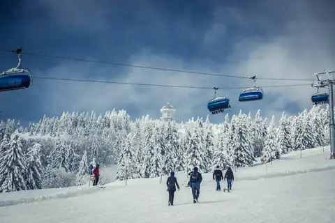 Blaue Gondeln der Feldbergbahn über verschneite Skipiste mit Wanderern und Skifahrern im Winter