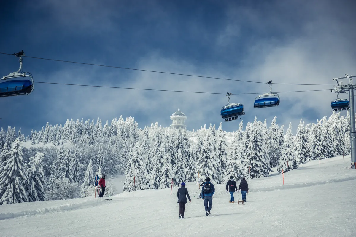 Blaue Gondeln der Feldbergbahn über verschneite Skipiste mit Wanderern und Skifahrern im Winter