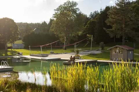 Naturbadesee mit Steg, Liegewiese und Waldkulisse im Abendlicht