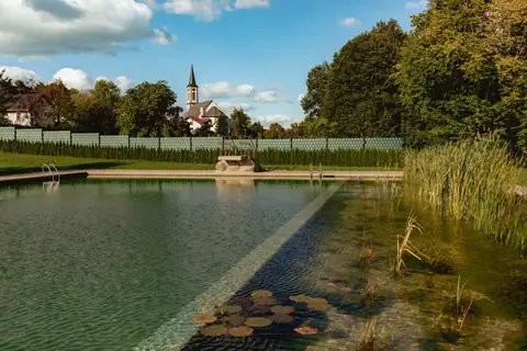 Naturfreibad mit Schwimmbereich, Schilfzone und Kirchturm im Hintergrund