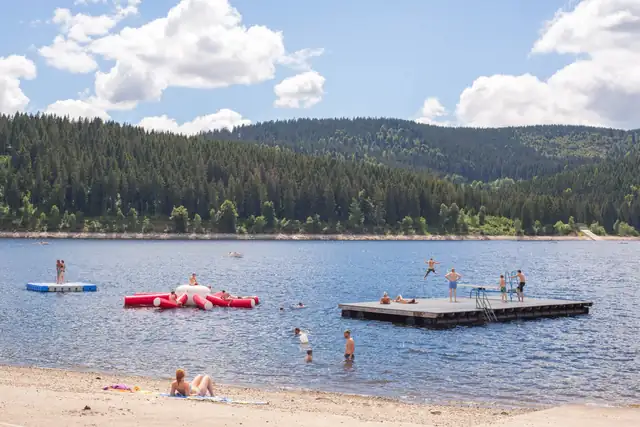 Badestrand am Schluchsee mit Wasserspielgeräten, Badesteg und Schwimmern, dahinter bewaldete Hänge