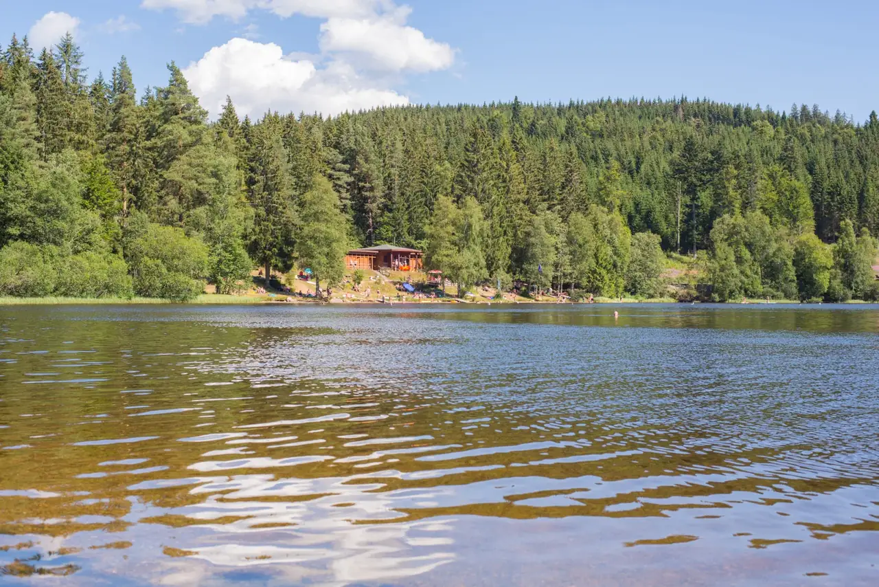 Blick über den Windgfällweiher auf das hölzerne Strandbad am bewaldeten Ufer