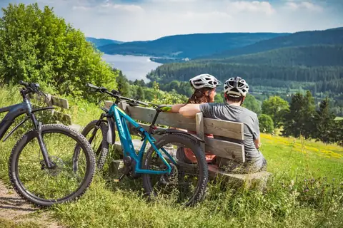Radfahrerpaar mit E-Bikes auf Bank mit Blick auf den Schluchsee
