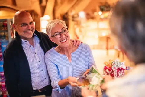 Zwei Besucher lassen sich an einer Ladentheke Süßwaren zeigen