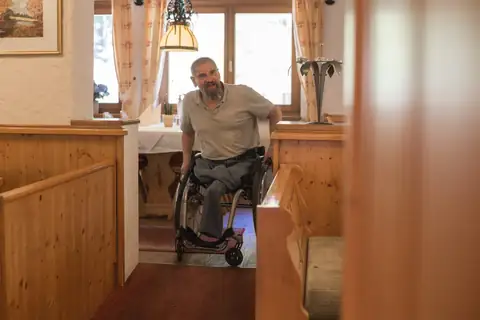 Rollstuhlfahrer in gemütlicher Gaststube mit Holzvertäfelung und Fensterplatz