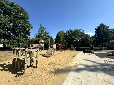 Spielplatz mit Holzklettergerüst, Schaukel und Sandfläche neben der Minigolfanlage