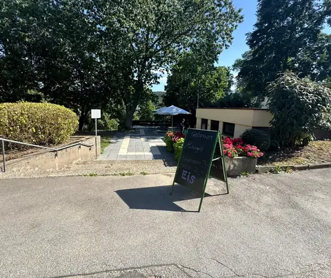 Eingang zur Minigolfanlage mit Aufsteller und Blumenbeet, dahinter das Minigolfcafé