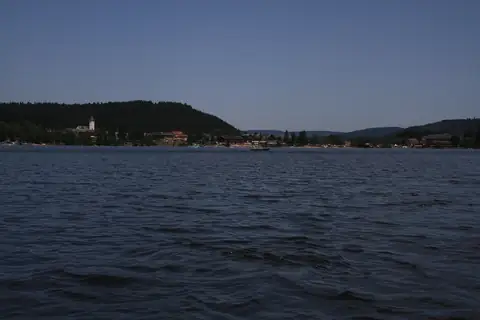 Titisee mit Blick auf die Uferpromenade und Kirchturm, umgeben von bewaldeten Hügeln