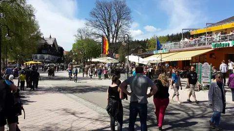 Belebte Fußgängerzone in Titisee mit Touristen, Cafés und Geschäften bei Sonnenschein