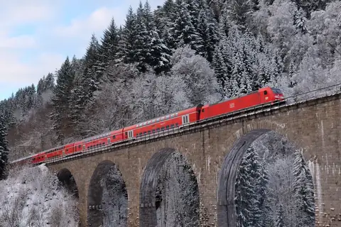 Roter Doppelstock-Regionalzug der DB auf einem steinernen Viadukt im winterlich verschneiten Schwarzwald