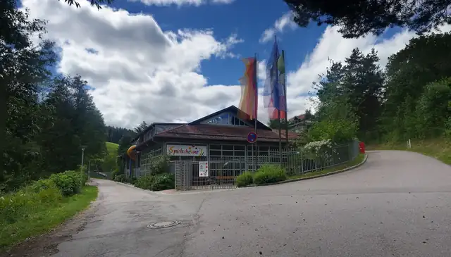 Eingangsbereich der Spielscheune mit buntem Schriftzug, Rutschenturm und Fahnen vor blauem Himmel