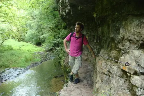Wanderer auf schmalem Felsenpfad mit Stahlseil-Sicherung neben einem Bach in der Gauchachschlucht
